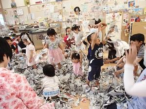 ビリビリに破いた新聞紙を、床に散らした中に子ども達が入り遊んでいる写真