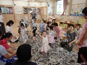 母親たちが座っているなかに、ビリビリに破いた新聞紙の中に入って子供たちが新聞紙を散らかして楽しそうに遊んでいる様子の写真