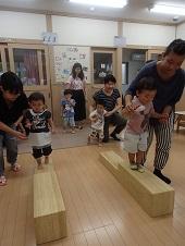 2つの木製の平均台が平行に並んでそれぞれ母親が付き添いながら、2名の子どもが渡っている写真