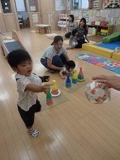 カラフルな色のボウリングのピンの前で黄色の輪っかをピンに入れた女の子を支えている母親、ピンに輪っかを入れてプレゼントをもらおうとしている男の子の写真