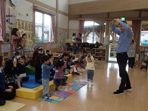 両手を挙げて丸の形を作って手遊びをしている先生と子供たちの写真