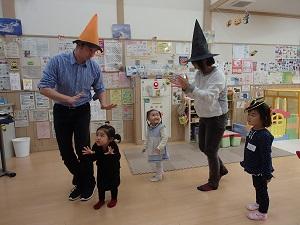 立ち上がってダンスをしている、オレンジ色の帽子をかぶった先生と3人の子供と黒い帽子をかぶった母親の写真