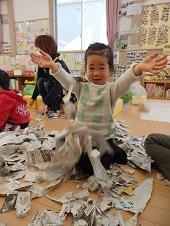 びりびり破いた新聞紙の中に座っている女の子が両手でぱ～っと破った新聞紙を散らした瞬間の写真