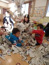ビリビリに破った新聞紙の中に埋もれている男の子とその横で新聞紙を勢いよく放り投げている男の子の写真
