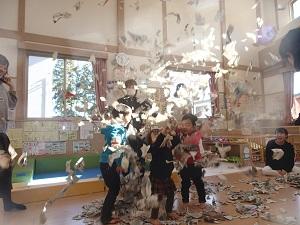 舞い上がった新聞紙の中で子供達が大はしゃぎをしている様子の写真