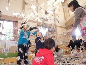男の子2人が立ち上がってびりびり破いた新聞紙を上に放り投げ、沢山の新聞紙が舞い上がっている様子の写真