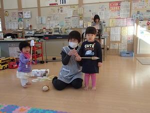手に棒を持った二人の子供とその間に子育て支援センターの職員の方が座っている様子の写真