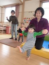 母親の両手を握り足を挙げる子供の写真