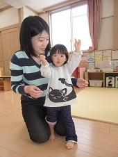 母親の隣で両手を挙げる子供の写真