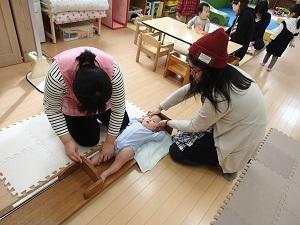 床の上で赤ちゃんの伸長をはかる女性と、赤ちゃんの頭を支える女性の写真