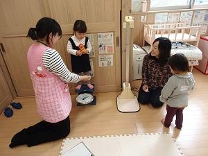 女の子が体重計の上に立ち、エプロンを着た女性が女の子の方へ手を伸ばしている写真