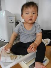 体重計の上に座っている赤ちゃんが自分の足を触っている写真