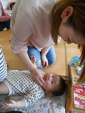 ほっぺたを触る女性を、仰向けに寝ている赤ちゃんが見つめている写真