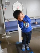 体重計の上に立っている男の子が、両手を左頬にあて左に傾くポーズをとっている写真