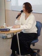 椅子に座っている臨床心理士の女性がマイクを持って話をしている写真