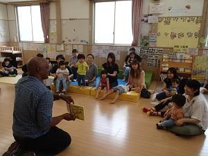 絵本の読み聞かせをしている英語の先生と座って話を聞いている子供たちの写真