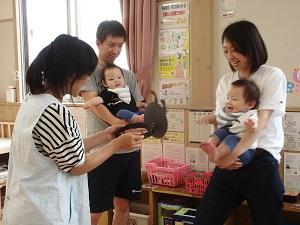 2組の親子が赤ちゃんを背後から抱いており、歯科衛生士さんがバイキンマンのお面を赤ちゃんに見せて、赤ちゃんがお面に喜んでいる様子の写真