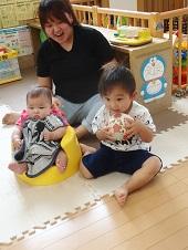 笑顔のお母さんの前で、ボールを持って座っている男の子と椅子に座っている赤ちゃんの写真