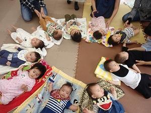 子育て支援センターの床の上に広げたタオルの上に、円状に並べられた11人の赤ちゃんの集合写真