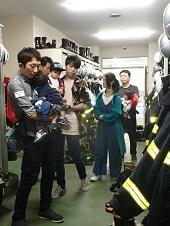キャビネットにヘルメットや消防服が掛けてある場所を見学する参加者の写真