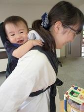 母親に抱っこ紐で背負われて笑顔の赤ちゃんの写真