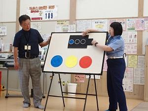 ボードの左側に男性、右側に女性警察官が立ち、ボードに色が変わる色画用紙で作った信号と、丸型の赤・青・黄の信号が貼られているパネルシアターの様子の写真