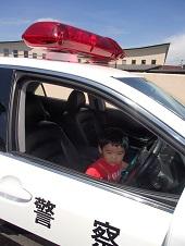 赤色のシャツを着た男の子が運転席に座って、やや緊張気味の様子の写真