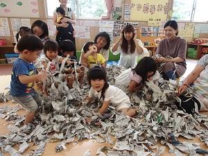 大量の新聞紙の紙片を掴んで遊ぶ子供たちの写真