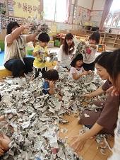 新聞紙の紙片だらけになった床に座る子供たちと保護者の写真