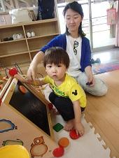 子育て支援センターにあるおもちゃで遊ぶ子供と、それを見ている母親の写真