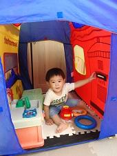 テントの中に入り鍋のおもちゃで遊んでいる子供の写真