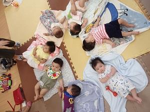 7名の赤ちゃんが放射線状にブランケットの上に寝そべっている写真