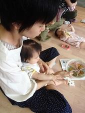 赤ちゃんを膝の上に座らせた母親が、右手で離乳食が入ったお皿を持って見ている写真