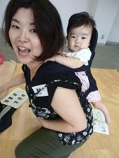中腰で座った母親が、抱っこ紐を使って赤ちゃんを背負っている写真