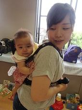 抱っこ紐で背負った赤ちゃんを笑顔で見ている母親の写真