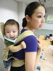 ベージュ色の抱っこ紐で背負った笑顔の赤ちゃんと母親の写真