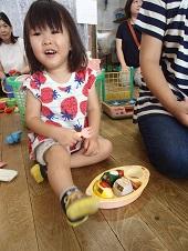 おもちゃのお皿にご馳走が盛り付けられ、笑顔の女の子がフォークを持っている写真
