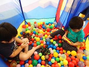 カラーボールやおもちゃが入っている網テントの中で遊ぶ2人の男の子の写真