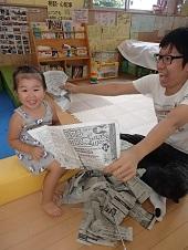 女の子とお父さんが新聞紙で遊び、ニコニコ笑顔で笑っている写真