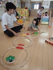 電車のおもちゃで遊んでいる女の子が横に座っているお父さんを見ている写真