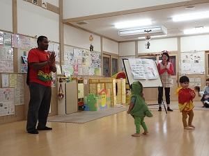 両手を合わせて立っている外国人の先生と保育士、ハロウィンコスチューム着ている子供たちの写真