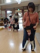 あ母さんが子どもの両手を持って、子供たちがお母さんの足の上に自分の足を乗せて一緒に歩いている写真