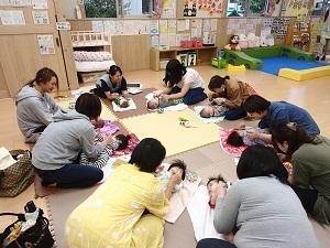 床の上にタオルを広げ仰向けの赤ちゃん達と笑顔でベビーマッサージを楽しむ参加者達の写真