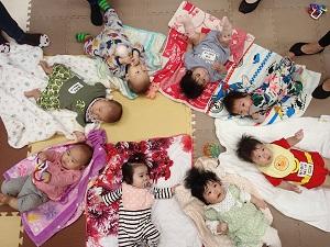 円状に広げたタオルの上に、仰向けに寝かされている8人の赤ちゃん達の写真