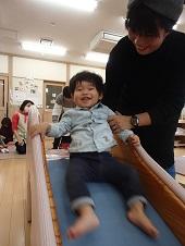 手すりを掴み、笑いながら滑り台を滑っている子供と、子供の腕を掴んでいる保護者の写真