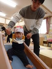 保護者に手を持ってもらい滑り台を滑る子供の写真