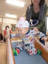 滑り台で足を延ばす赤ちゃんと、後ろから赤ちゃんを掴んでいる保護者の写真