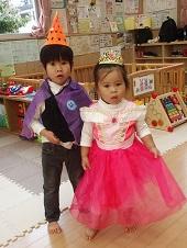 ティアラを頭にのせてピンク色のドレスを着た女の子とオレンジ色の三角帽子をかぶり紫色のマントを身につけた男の子の写真