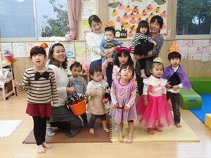オレンジ色のバケツを持っている英語の先生と子供たち、子供を抱いた母親の集合写真