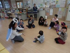 円を描くように輪になって座り手をたたいている英語の先生と親子の写真